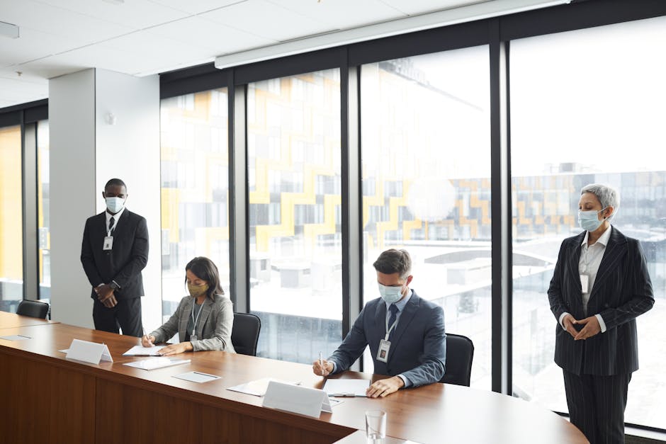 Colleagues in a meeting room wearing masks, signing documents at a modern office table.